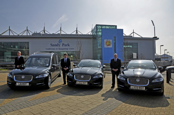 Jaguar XJ hearse and two Jaguar XJ limousines with three drivers alongside, outside Sandy Park Rugby Ground
